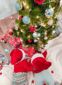 a small child is reading a book under the christmas tree