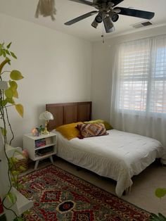 a bedroom with a bed, rug and ceiling fan in the corner next to a window