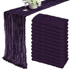 a purple table runner with white flowers and napkins on the top, along with two vases