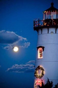 a lighthouse with christmas lights on it and the moon in the background