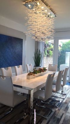 a dining room table with white chairs and a chandelier hanging from the ceiling