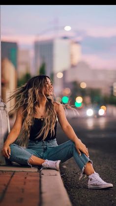 a woman is sitting on the curb with her hair blowing in the wind