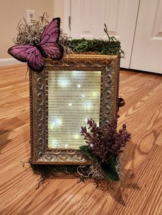 a purple butterfly sitting on top of a wooden floor next to a framed piece of paper