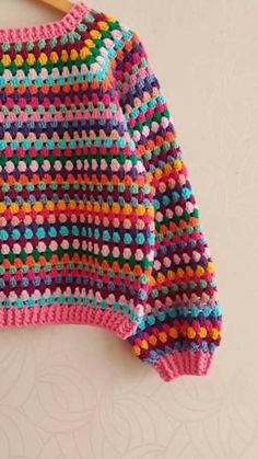 a crocheted sweater hanging on a wooden hanger, with colorful dots and circles