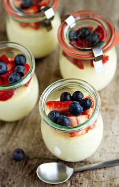 four small jars filled with fruit on top of a wooden table next to spoons