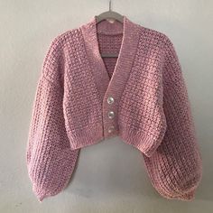 a pink knitted cardigan hanging on a white wall next to a wooden hanger