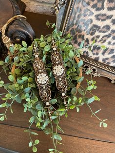 a vase filled with green plants next to a framed mirror on top of a wooden table