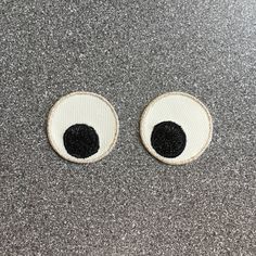 two black and white eyes are shown on a gray surface, one is in the shape of an eye