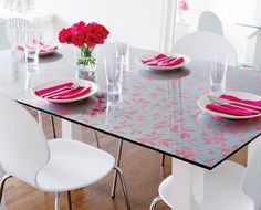 the table is set with white chairs and pink napkins on it, along with red flowers