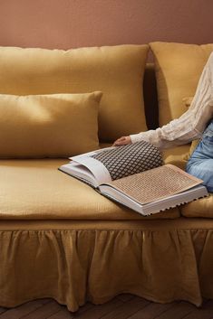 a person sitting on a couch with a book in their lap and pillows behind them