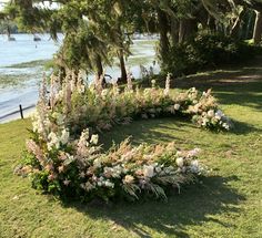 a circular arrangement of flowers in the grass near water with trees and boats in the background