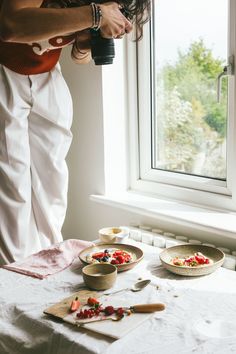 a woman standing in front of a window holding a camera over two plates with food on them