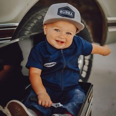 a baby sitting in the back of a truck wearing a hat and blue overalls