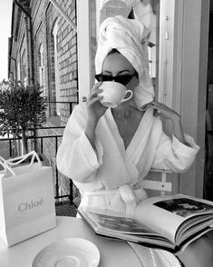 a black and white photo of a woman with a towel on her head drinking from a cup