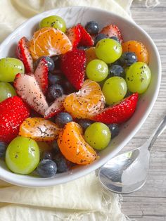 a white bowl filled with fruit on top of a table next to a fork and spoon