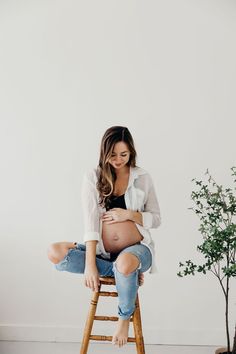 a pregnant woman sitting on top of a wooden stool