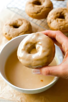 a hand holding a donut over a bowl of doughnuts