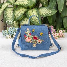 a blue handbag with flowers on it sitting in front of some potted plants