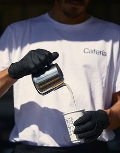 a man pouring something into a cup with black gloves on his arm and the other hand