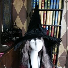 a white mannequin head wearing a black witch's hat in front of bookshelves