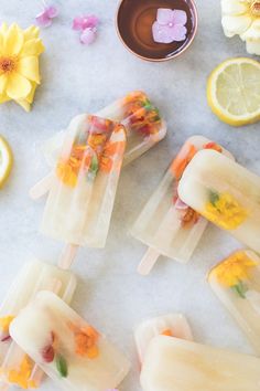 four popsicles with flowers on them sitting next to lemon slices