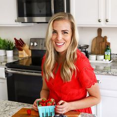 a woman in a red dress holding a bowl of strawberries on a kitchen counter