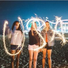 three girls are standing on the beach holding sparklers