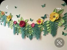 paper flowers and leaves are hanging on the wall with butterflies flying around them in the background