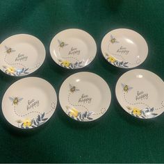 six white plates with bee designs on them sitting on a green cloth covered tablecloth