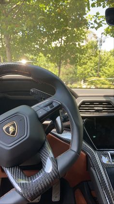 the steering wheel and dashboard of a luxury sports car with trees in the back ground