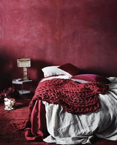 a bedroom with red walls and white bedding, two pictures hang on the wall