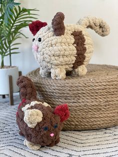 two small crocheted animals sitting on top of a round basket next to a potted plant