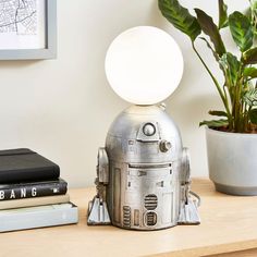 a silver robot lamp sitting on top of a wooden table next to a potted plant