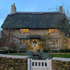 a stone house with a thatched roof and white gate