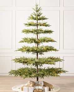 a small christmas tree with presents under it on a wooden floor in front of a white wall