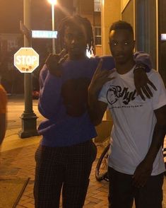 two young men standing next to each other in front of a stop sign at night