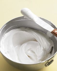 a bowl filled with white cream sitting on top of a table next to a knife