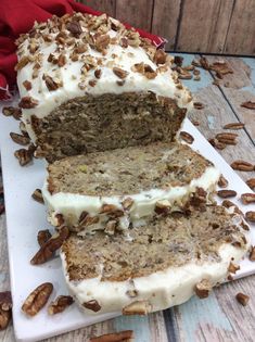 a loaf of carrot cake with white frosting and pecans around it on a cutting board