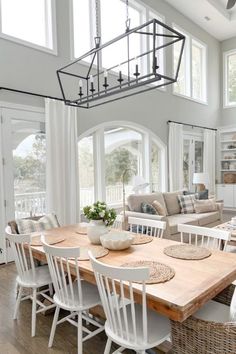 a dining room table surrounded by chairs and couches in front of two large windows