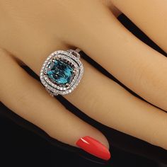 a woman's hand with red nail polish holding a blue and white diamond ring