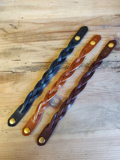 three different types of braided leathers on a wooden table with gold studded handles