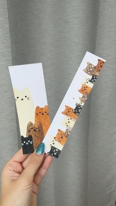 a person holding up two pieces of paper with cats and bears on them in front of a curtain