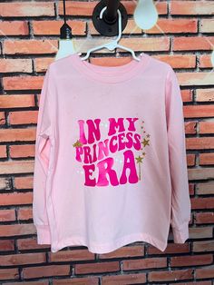 Calling all princesses! If you are in your official princess era, this long sleeve tee is a must have!  Text is in the trendy wavy style, with some white and gold glitter accents (don't worry - glitter will NOT come off!)  And a gold shimmer is all over the front and back of the shirt for that extra sparkle that every princess needs!  This makes a special birthday gift!!  Shirts are unisex fit and pre-shrunk.  https://hilhandmadeit.etsy.com Please Read Before Purchase!  If you are looking for so Pink Birthday Top With Text Print, Pink Birthday Tops With Text Print, Pink Tops With Text Print For Birthday, Pink Long Sleeve Top For Birthday, Pink Glitter Print Top For Birthday, Pink Long Sleeve T-shirt With Name Print, Princess Era, Wavy Style, Special Birthday Gifts