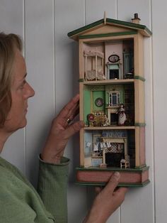 a woman is looking at a dollhouse on the wall in front of her house