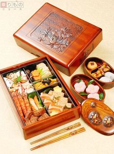 an assortment of sushi in wooden boxes with chopsticks on the table next to it