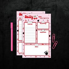 the daily planner is next to a pink pen on a black surface with red writing