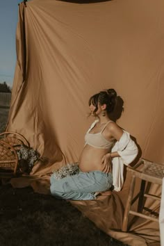 a pregnant woman sitting on top of a wooden chair next to a brown tarp