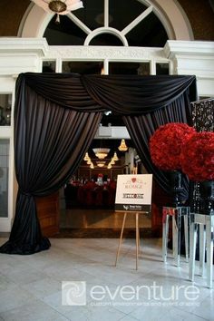 the entrance to an event with black drapes and red flowers in vases on display