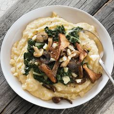 a white bowl filled with mashed potatoes covered in mushrooms and spinach on top of a wooden table