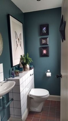 a white toilet sitting in a bathroom next to a sink and mirror with pictures on the wall